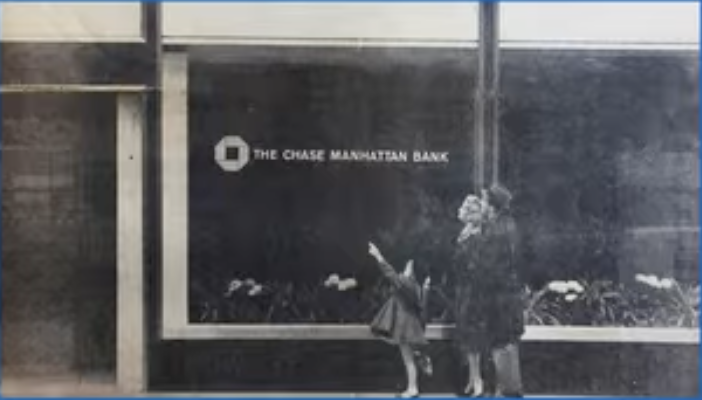 Newspaper photo of a woman and a small girl pointing up at the new octagon logo on a Chase Manhattan Bank window.